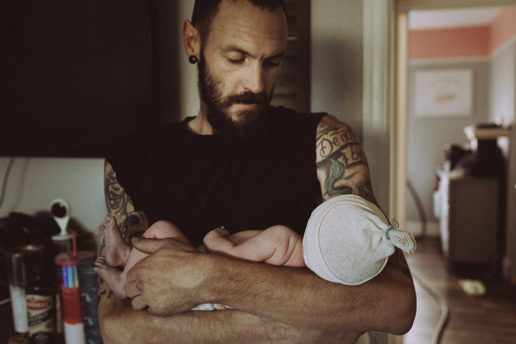 Dad holding brand new baby girl in arms in their home after home birth 