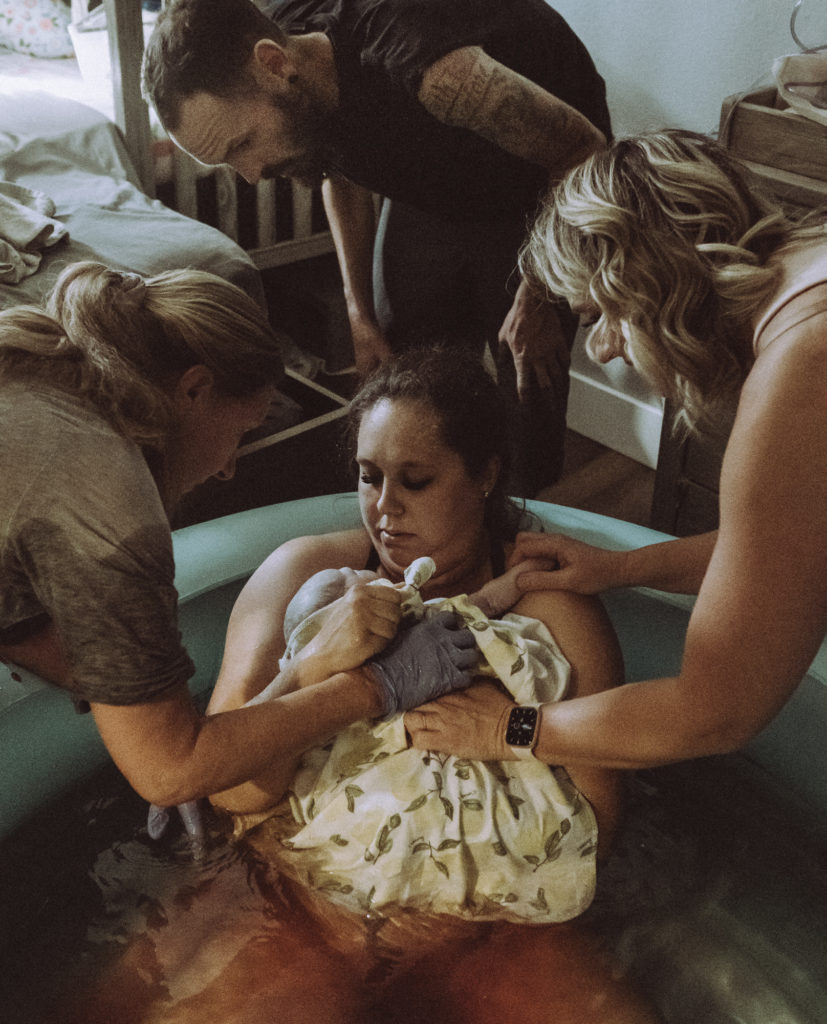 Dad, doula, and midwife all gazing at freshly born baby during home birth 